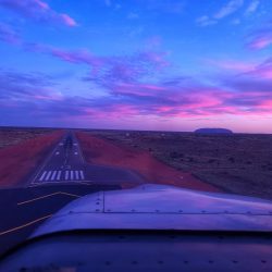 Landing at Ayers Rock at dusk with rosy pink and purple hues, gorgeous Uluru in the background